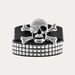 Ceinture homme cloutée tête de mort grand format avec strass fixée sur une ceinture en simili-cuir noir, le tout sur fond uni.