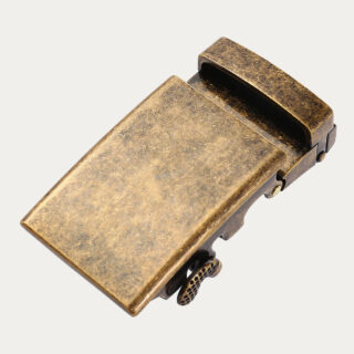 Une boucle ceinture automatique homme style vintage et patinée de couleur bronze sur un fond gris très clair uni.