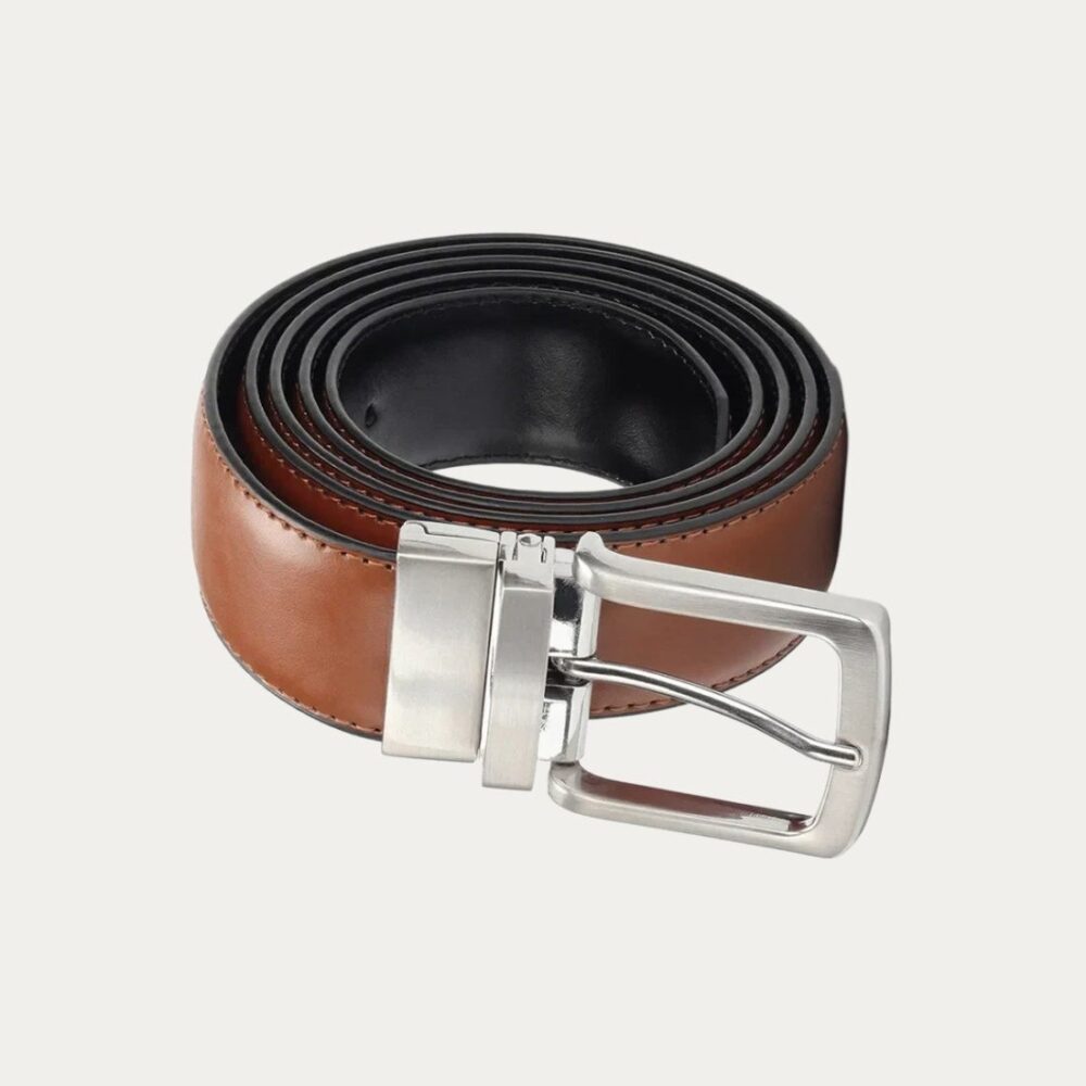 Une ceinture réversible homme à boucle argentée de couleur marron enroulée sur elle même sur un fond gris très clair uni